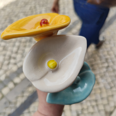 Três flores cerâmicas coloridas seguradas por uma mão em fundo de calçada portuguesa