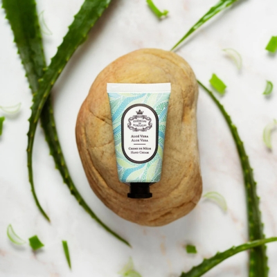 Creme de mãos em tubo com design azul e verde sobre pedra amarela e folhas de aloe vera