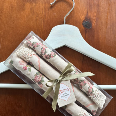 Conjunto de saquinhos perfumados de linho com padrão floral e renda em caixa transparente com laço dourado