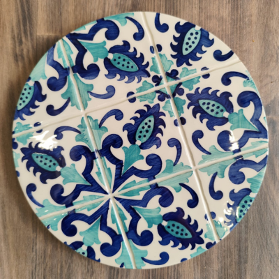 Prato decorativo redondo em cerâmica com padrão floral azul e verde sobre madeira