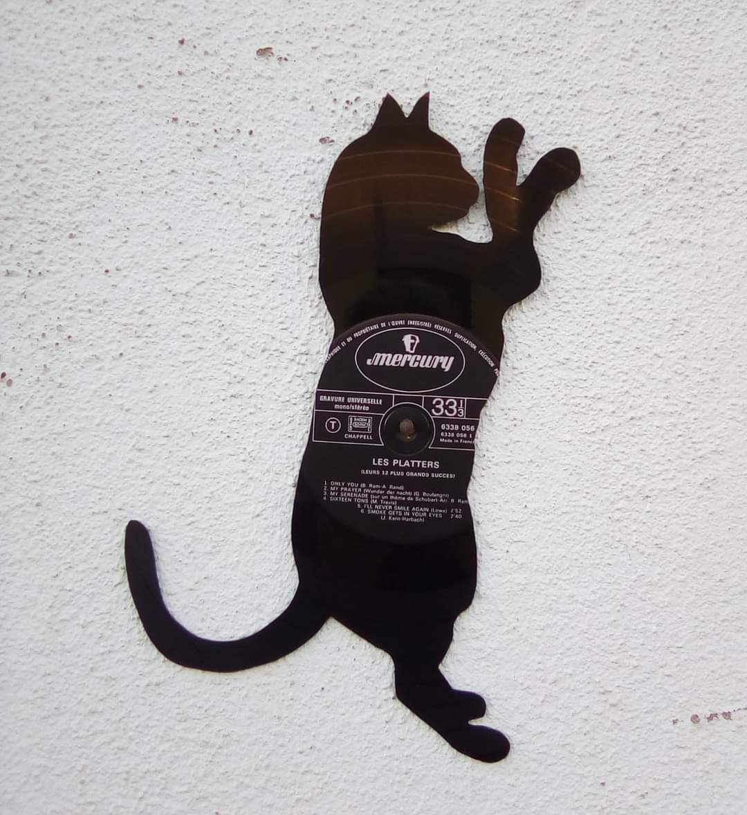 Silhueta de gato em metal preto com etiqueta redonda na parede branca