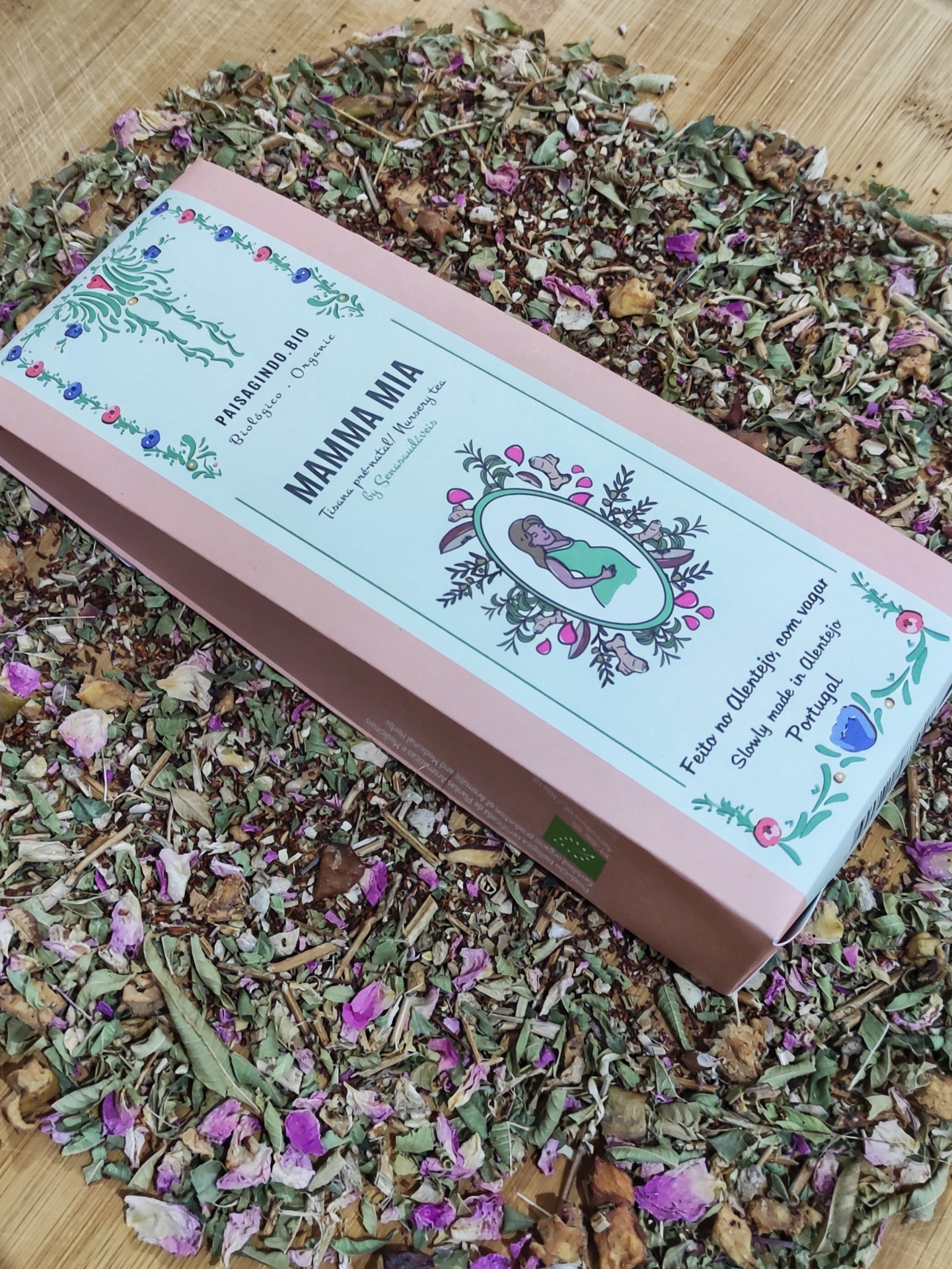 Caixa rosa de chá Mamma Mia rodeada por ervas secas e flores