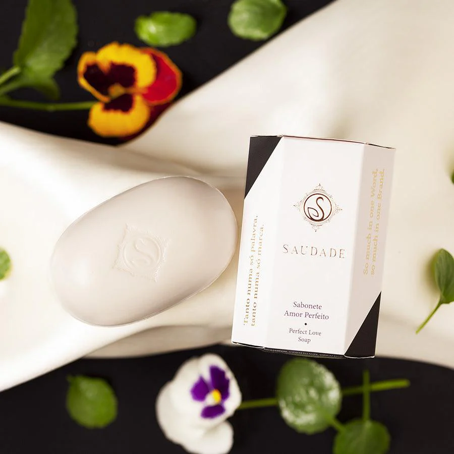 Sabonete branco oval com embalagem branca e preta e flores coloridas ao redor.