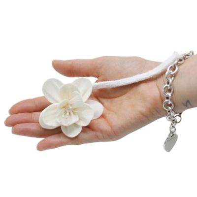 Mão com pulseira prateada segurando flor branca artificial