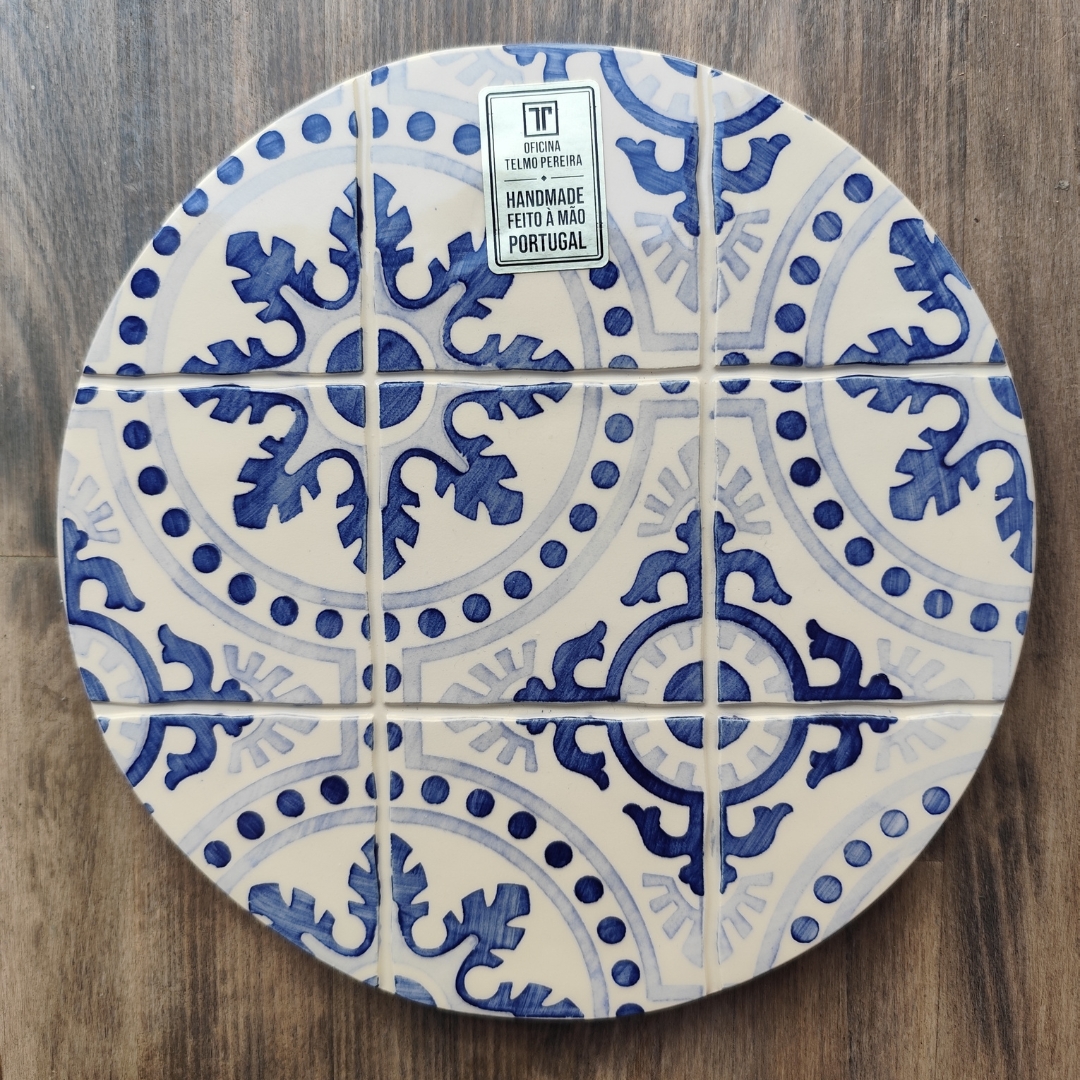 Prato redondo de azulejos azul e branco com etiqueta de fabricação manual em Portugal sobre madeira.