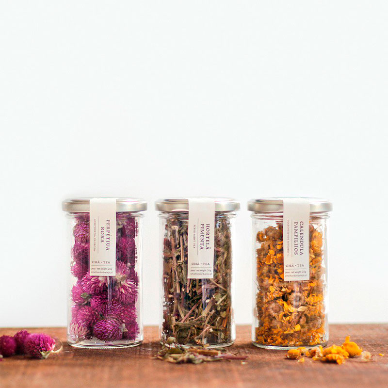 Três frascos com flores secas de diferentes cores e etiquetas em fundo branco