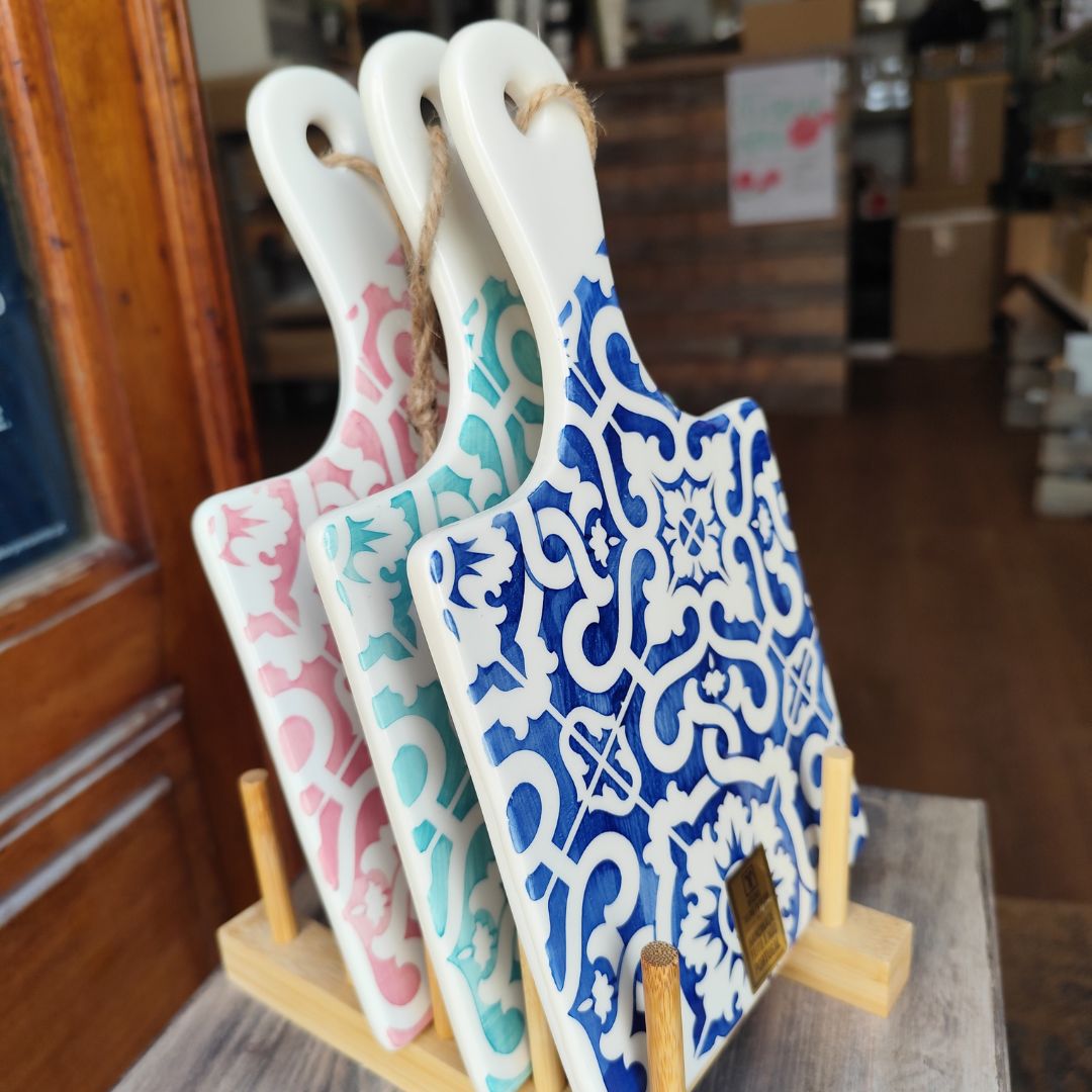 Três tábuas decorativas de cerâmica com padrão tradicional em azul, verde e rosa em suporte de madeira.