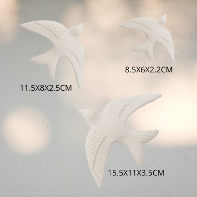 Ornamentos brancos de pássaros em voo com texturas de penas e dimensões etiquetadas pendurados numa parede branca