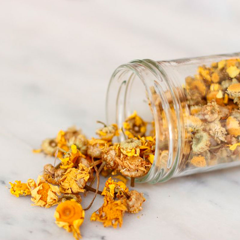 Frasco de vidro com flores secas amarelas e castanhas espalhadas