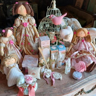 Bonecas de pano, frascos e sabonetes decorativos numa mesa com gaiola e flores de tecido