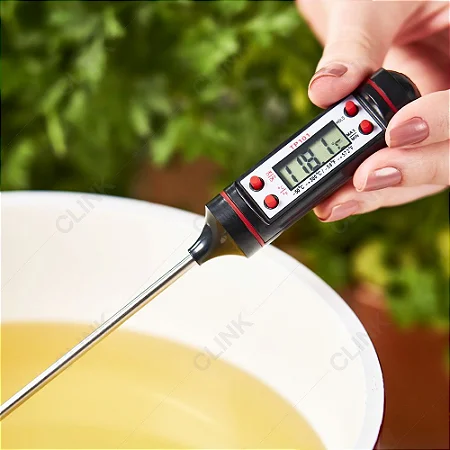 Termómetro digital preto e vermelho medindo temperatura de líquido amarelo em recipiente branco