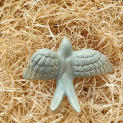 Objeto decorativo de cerâmica azul em forma de pássaro com asas abertas sobre palha