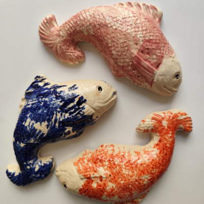 Três peixes cerâmicos decorativos coloridos em superfície branca