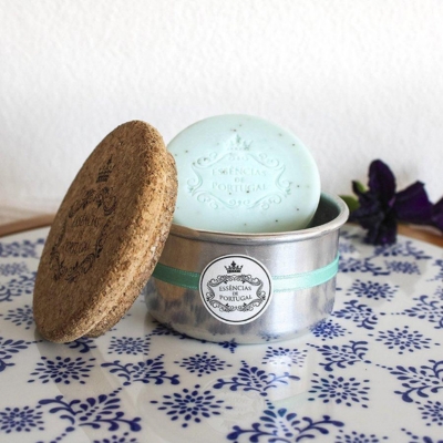 Sabonete azul claro numa caixa metálica com tampa de cortiça sobre pano azul com padrão branco
