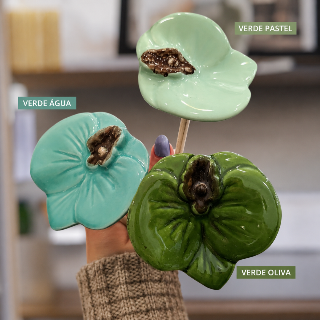 Três flores decorativas em cerâmica verde pastel, verde água e verde oliva seguradas por uma mão.