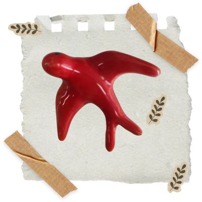 objeto decorativo vermelho em forma abstrata sobre papel branco com fita adesiva