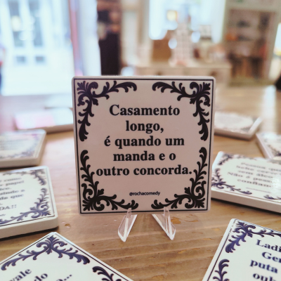 Peça decorativa branca quadrada com moldura azul escura e texto em português, sobre suporte em mesa de madeira
