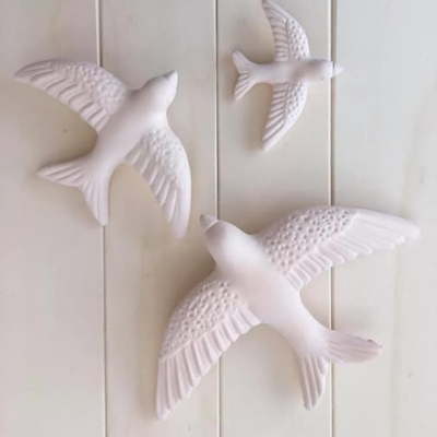 Três esculturas brancas de pássaros em diferentes tamanhos sobre fundo claro