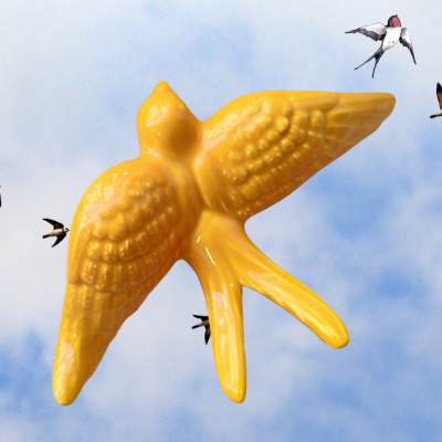 Pássaro amarelo em cerâmica com asas abertas no céu azul