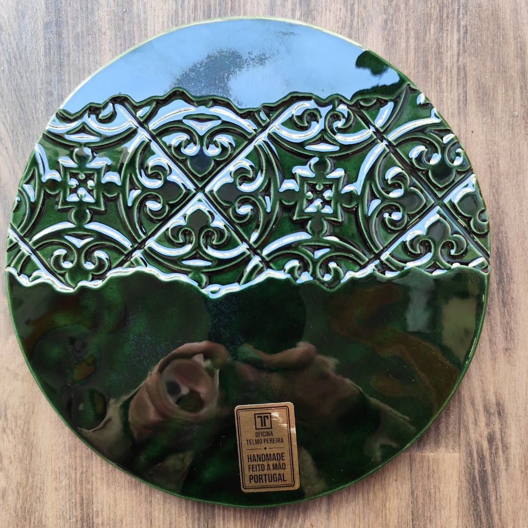 Prato redondo cerâmico verde com padrão decorativo em relevo e etiqueta dourada