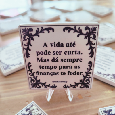 Azulejo branco quadrado com texto em português e moldura decorativa preta sobre suporte transparente