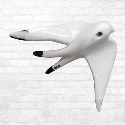 Escultura de cerâmica branca de gaivota com pontas pretas numa parede de tijolos brancos.