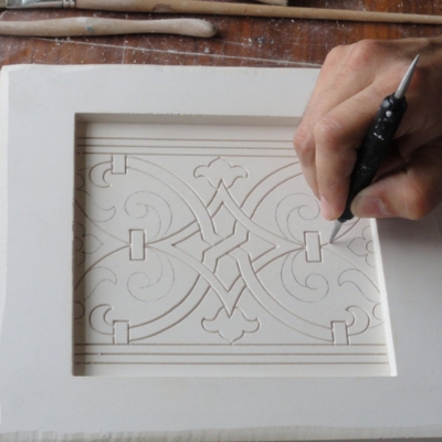 Escultura a trabalhar num desenho geométrico numa peça retangular branca