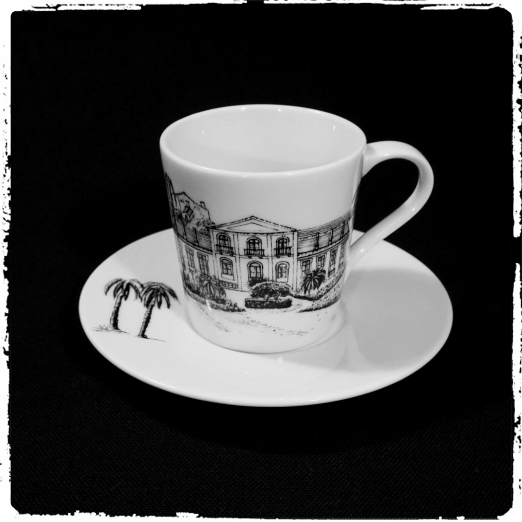 chávena e pires de porcelana branca com desenho a traço negro de edifício e palmeiras