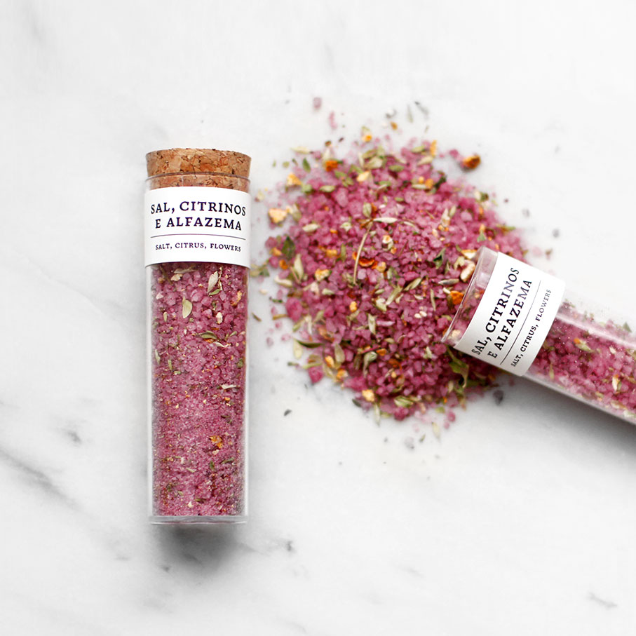 Tubetes de vidro com mistura de sal, citrinos e alfazema e tampas de cortiça sobre superfície branca