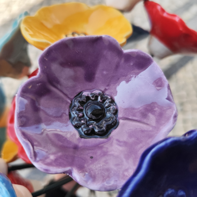 Flor decorativa em cerâmica roxa com flores amarelas, vermelhas e azuis ao fundo