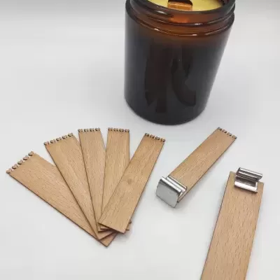 Vela acesa em frasco de vidro castanho com várias palhetas de madeira dentadas e duas com presilhas metálicas