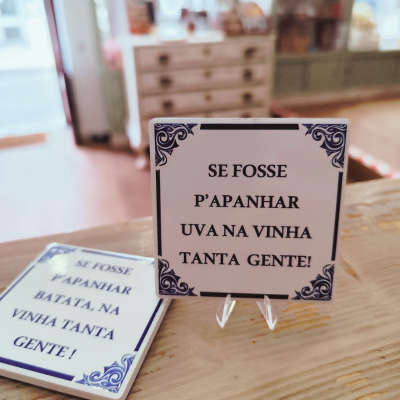 Dois azulejos decorativos quadrados com texto em português sobre uma mesa de madeira
