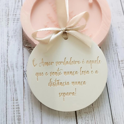 Placa decorativa redonda branca com texto em dourado e laço bege