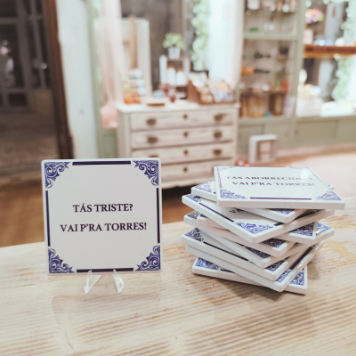 Azulejos decorativos brancos e azuis com texto em português numa mesa de madeira clara