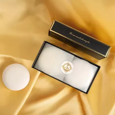 Caixa preta com lenço branco sobre tecido acetinado dourado