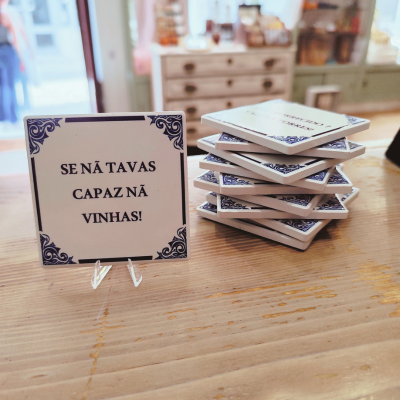 Placa decorativa branca com bordas azuis e texto preto em português sobre uma mesa de madeira