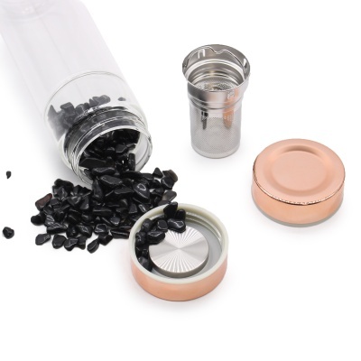 Frasco transparente com pedras pretas e acessórios metálicos em tom cobre sobre fundo branco