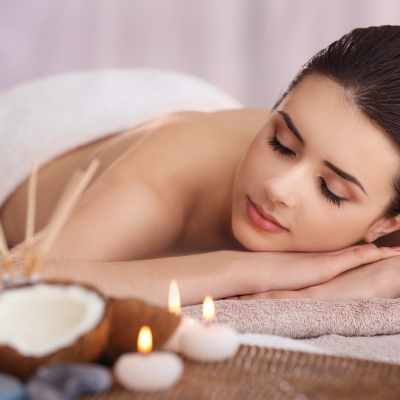 Mulher de olhos fechados deitada de bruços com velas e coco no primeiro plano