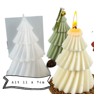 Velas em forma de árvore de Natal em branco e verde, uma acesa, com textura em camadas, etiqueta com sininho e embalagem branca ao fundo.
