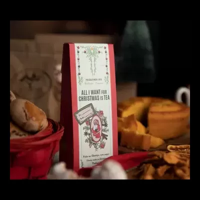 Pacote de chá vermelho com etiqueta branca decorada, rodeado de comida de Natal