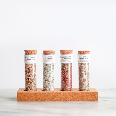 Conjunto de frascos de vidro com sal aromatizado em diferentes cores e texturas, tampas de cortiça, base de cortiça