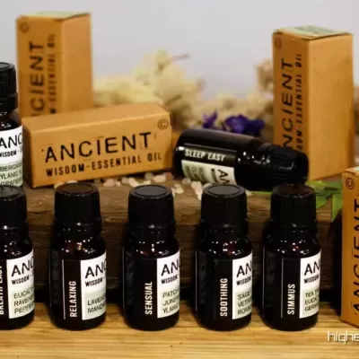 Frascos pretos e caixas castanhas claras de óleos essenciais ANCIENT WISDOM sobre madeira com flores