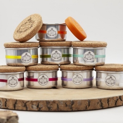 Potes metálicos com tampas de cortiça e faixas coloridas em suporte de madeira