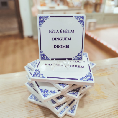 Azulejos cerâmicos brancos com padrão azul e texto em português num suporte sobre mesa de madeira