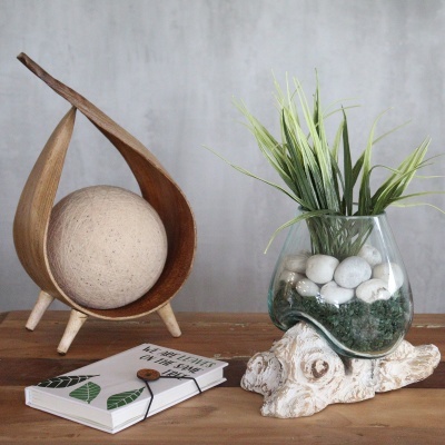 Objetos decorativos em madeira, vidro e planta artificial num ambiente minimalista