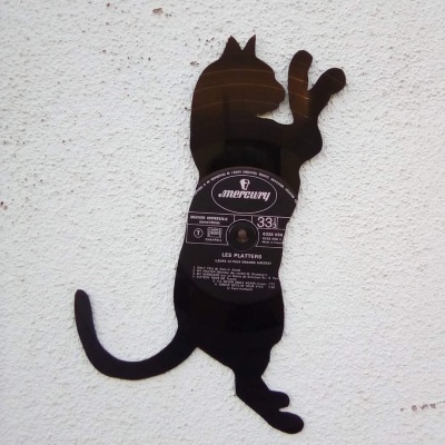 Silhueta de gato em metal preto com etiqueta redonda na parede branca