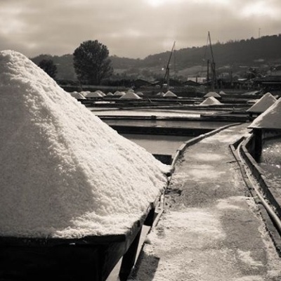 Montes de sal branco empilhados em estruturas ao ar livre com passadiços estreitos e cenário rural ao fundo