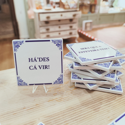 Azulejos quadrados brancos com texto em português e detalhes azuis, expostos sobre mesa de madeira