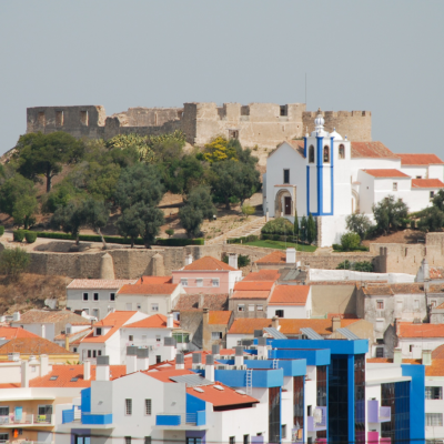 Cidade com casas brancas e vermelhas, igreja azul e branca e castelo antigo