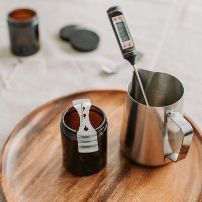 Frasco de vidro castanho, jarra metálica com termómetro digital numa bandeja de madeira